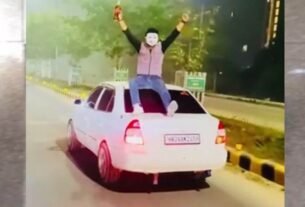 A young man wearing a mask sat on the roof of the car and waved a liquor bottle